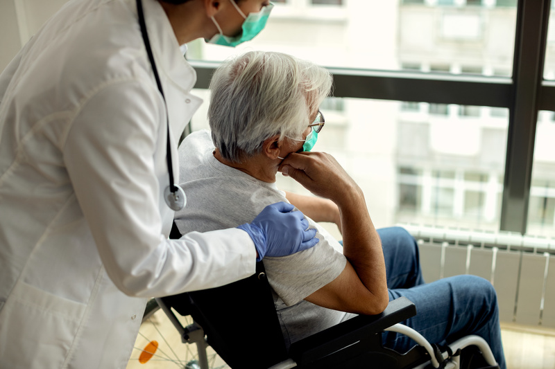 Female doctor consoling senior man in wheelchair during coronavirus lockdown.